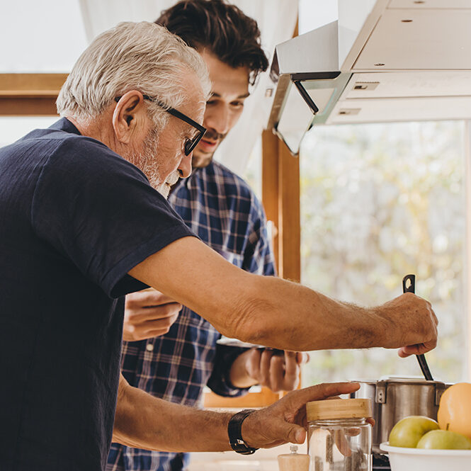 Senior man with younger man cooking in kitchen
